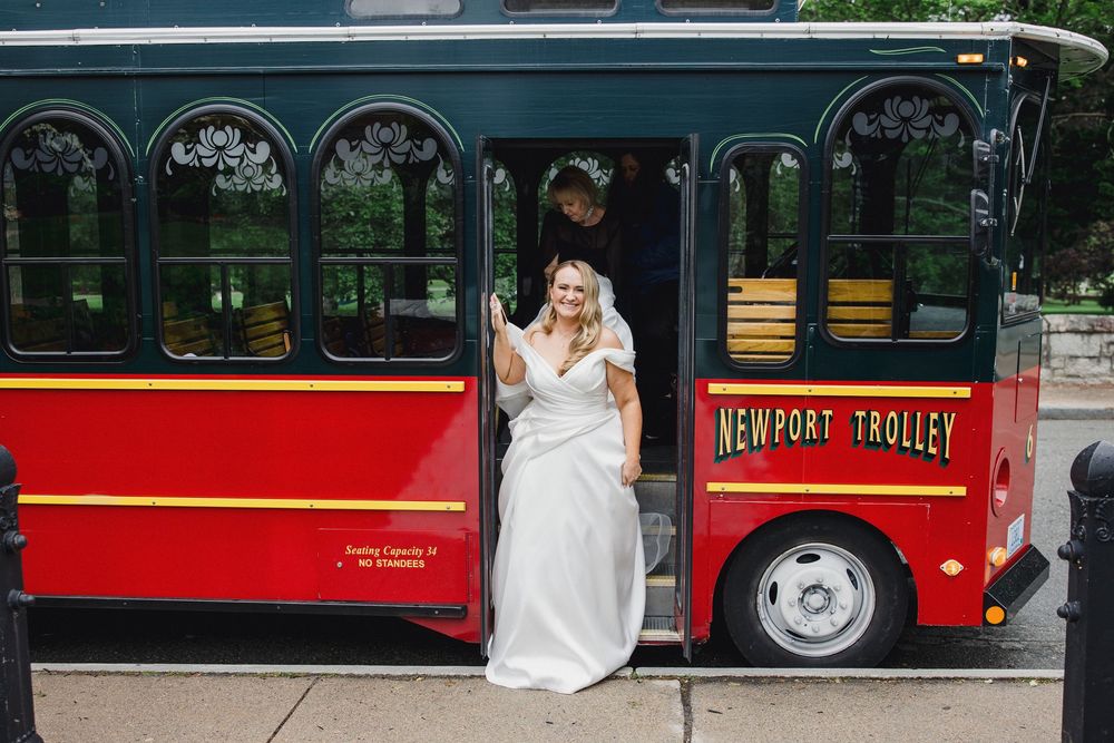 Wedding party posing beside red vintage trolley cars on a tree-lined street.