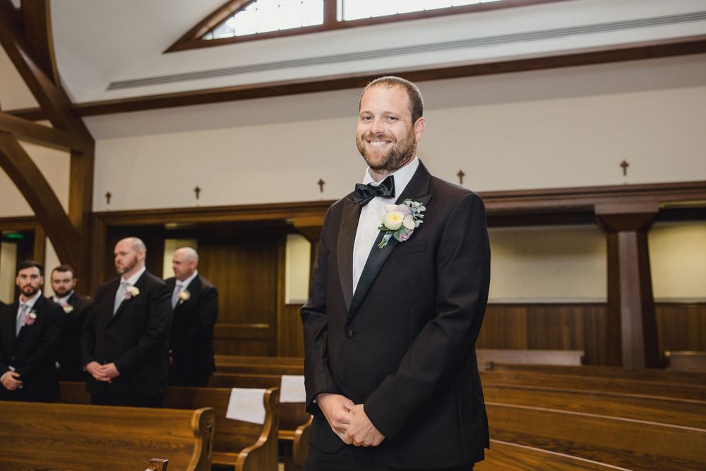 Couple exchanges vows at the altar of a classic church sanctuary with wooden pews and arched windows.