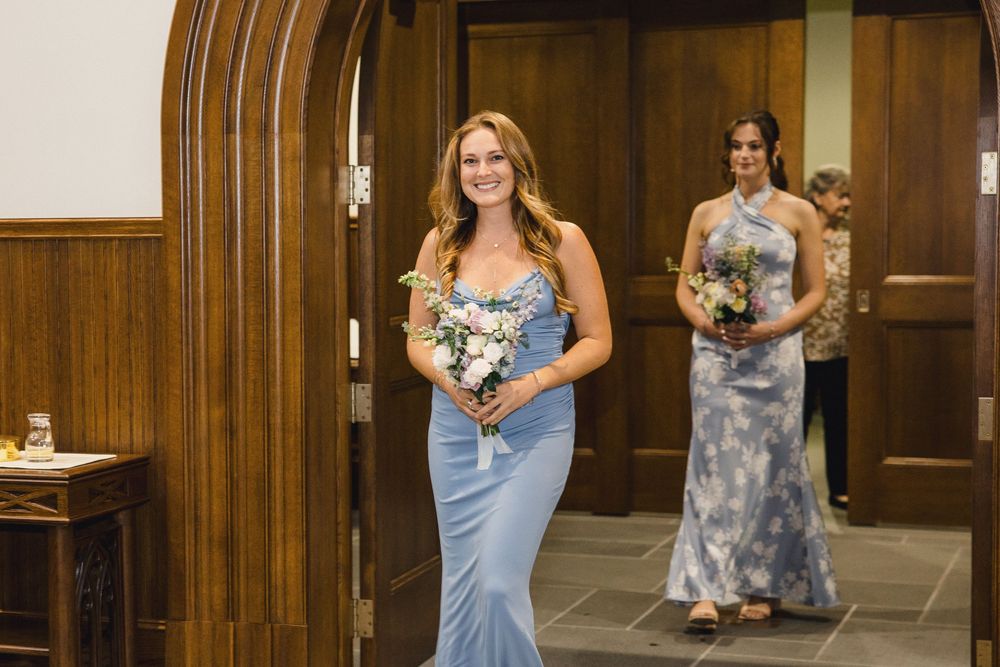 Wedding party members in blue dresses standing in a wood-paneled hallway.