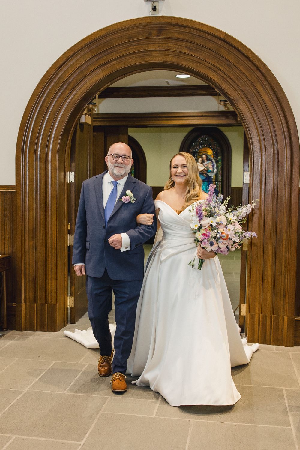 Wedding procession walking through elegant arched wooden doorways in a church.