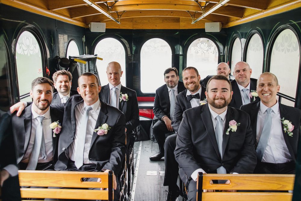 Wedding party members pose for candid photos in a rustic venue with wooden benches and warm lighting.