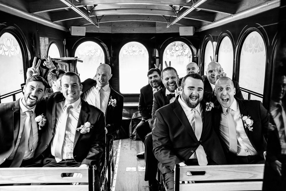 Wedding party laughing together while riding in vintage trolley bus in black and white photograph.