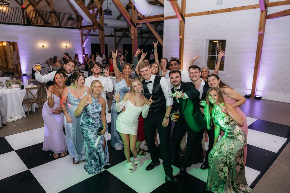 Wedding reception guests dance and celebrate on a crowded dance floor under warm lighting.