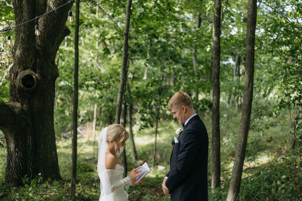 A couple shares their wedding vows during an intimate forest ceremony surrounded by lush green trees.