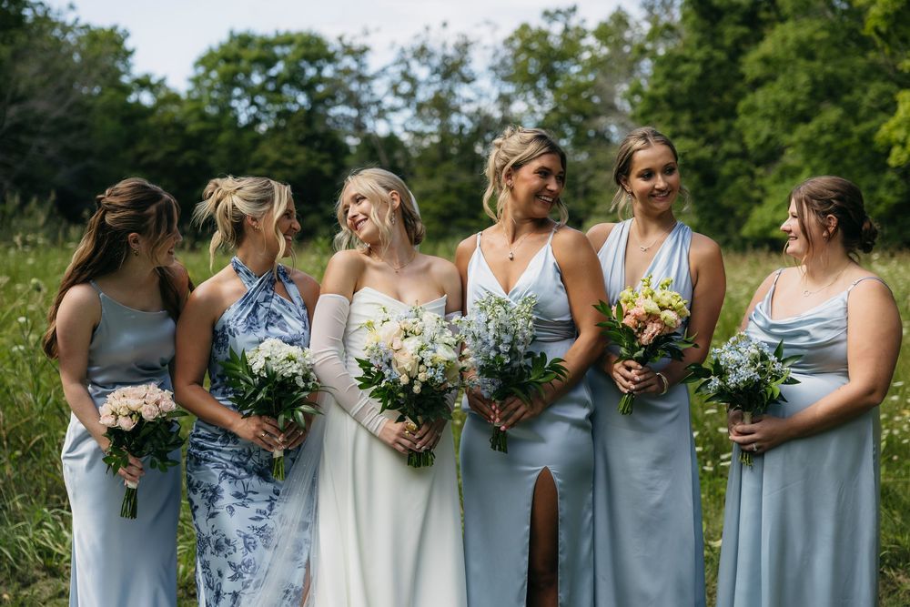 Bridesmaids in light blue dresses stand in a row holding white floral bouquets during an outdoor wedding ceremony.