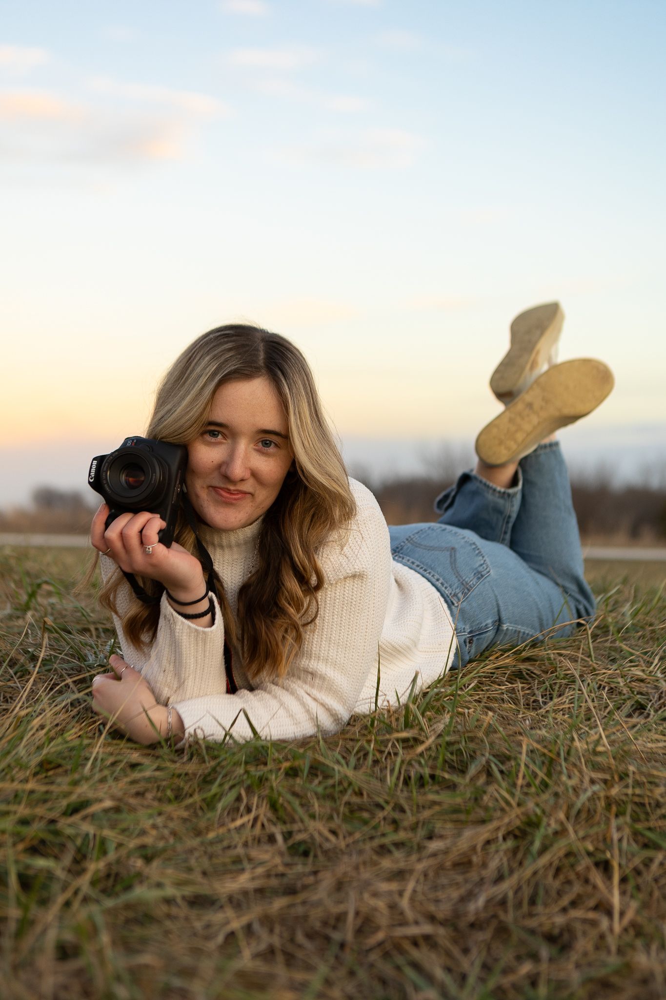 A photographer lying in dried grass with camera during golden hour.