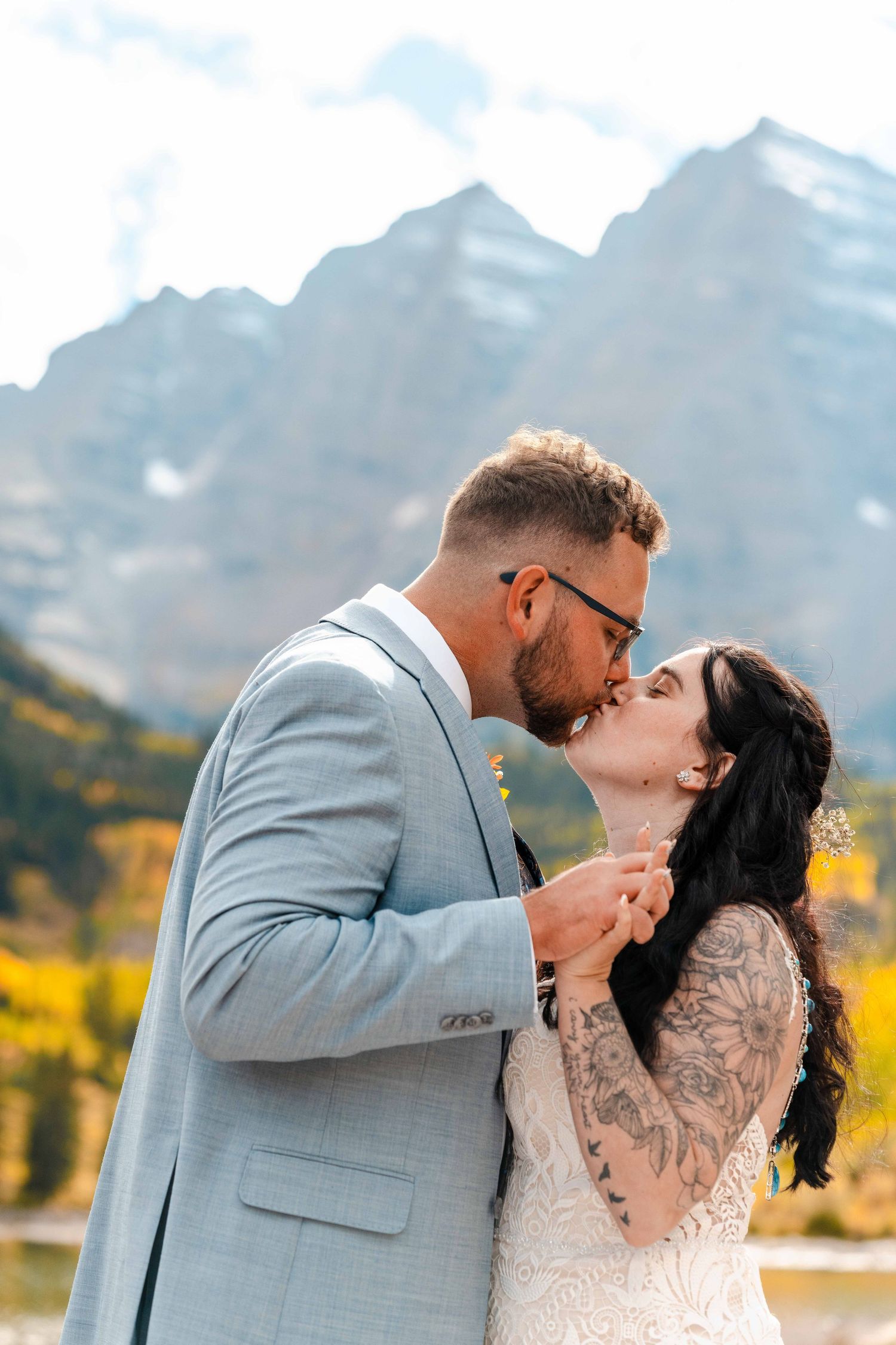Bride and groom kissing with snow-capped mountains and fall foliage in the background.