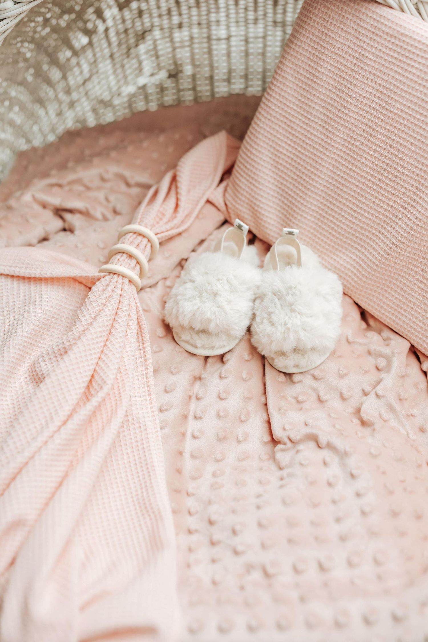 Soft pink baby booties and blanket create a delicate nursery scene with textured fabric and gentle lighting.