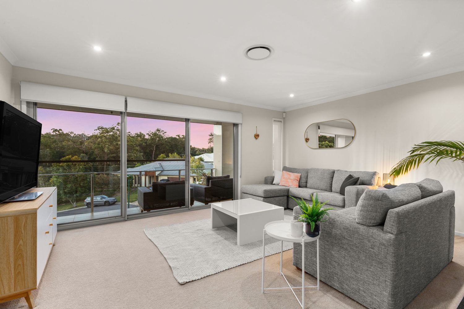 Comfortable upstairs living area with grey sofas, balcony access, and warm sunset views through glass doors.