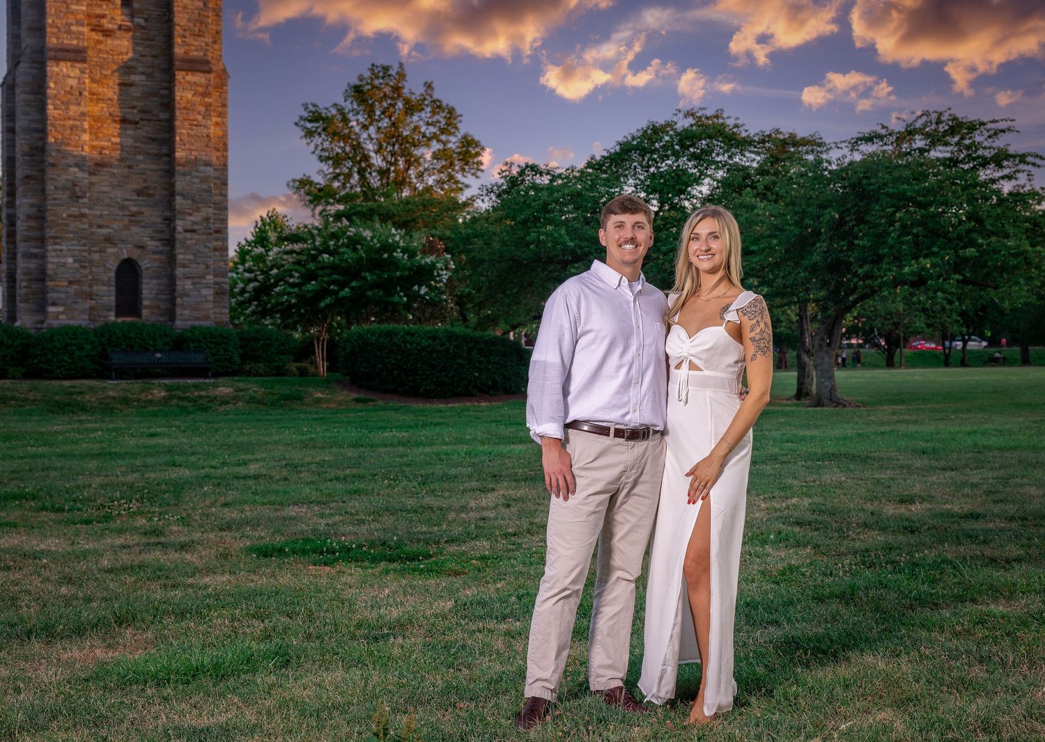 A couple poses together outdoors at sunset against a stone building backdrop.