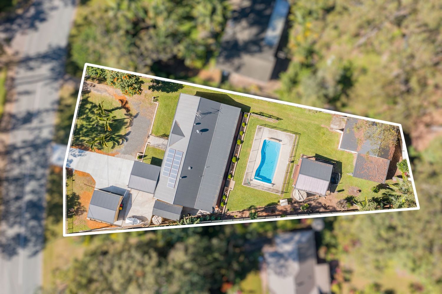 Aerial view of elongated residential property featuring inground pool, manicured lawns, and bushland surroundings.