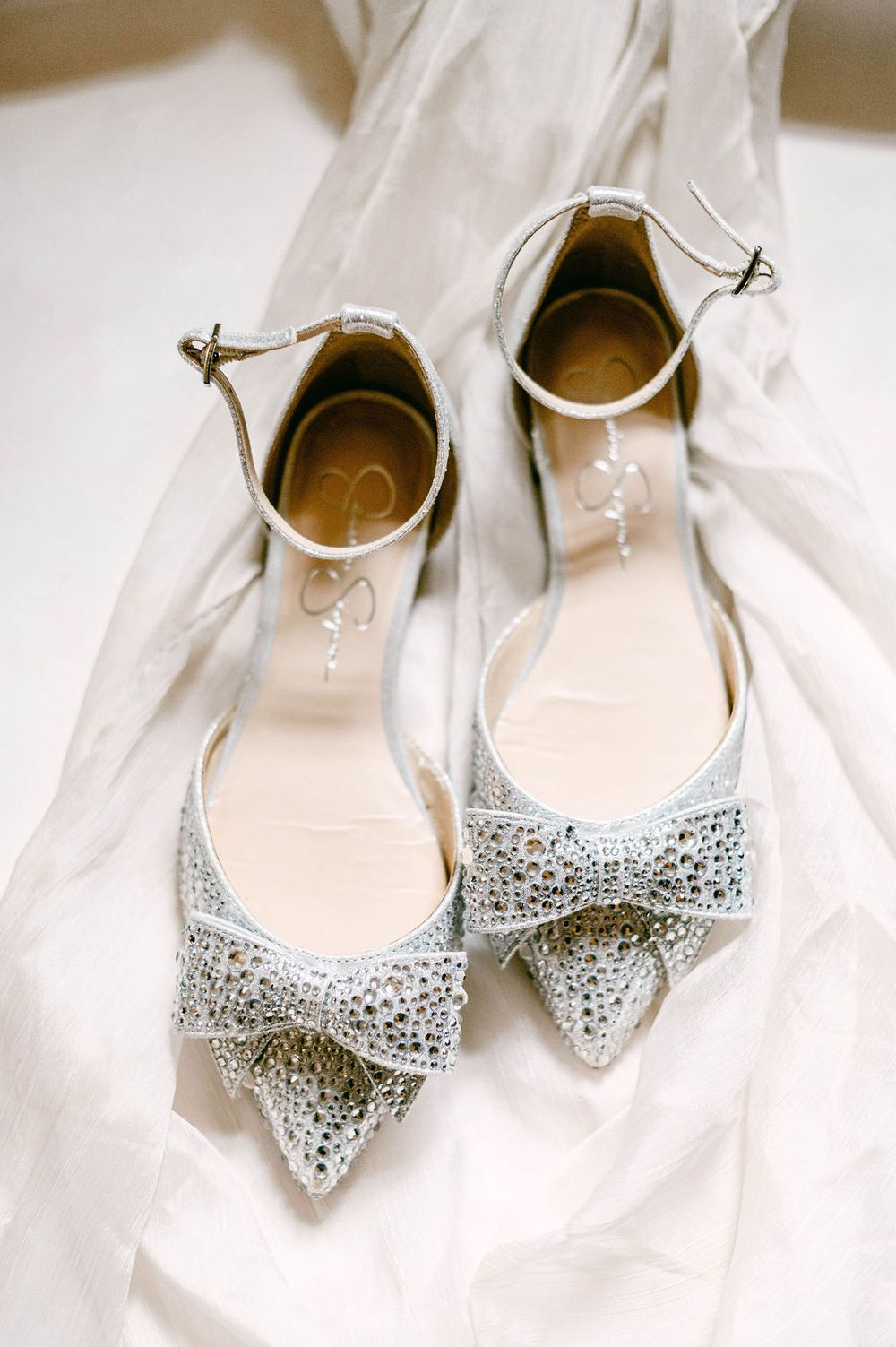 Elegant bridal shoes with sparkly crystal bows displayed on white fabric.