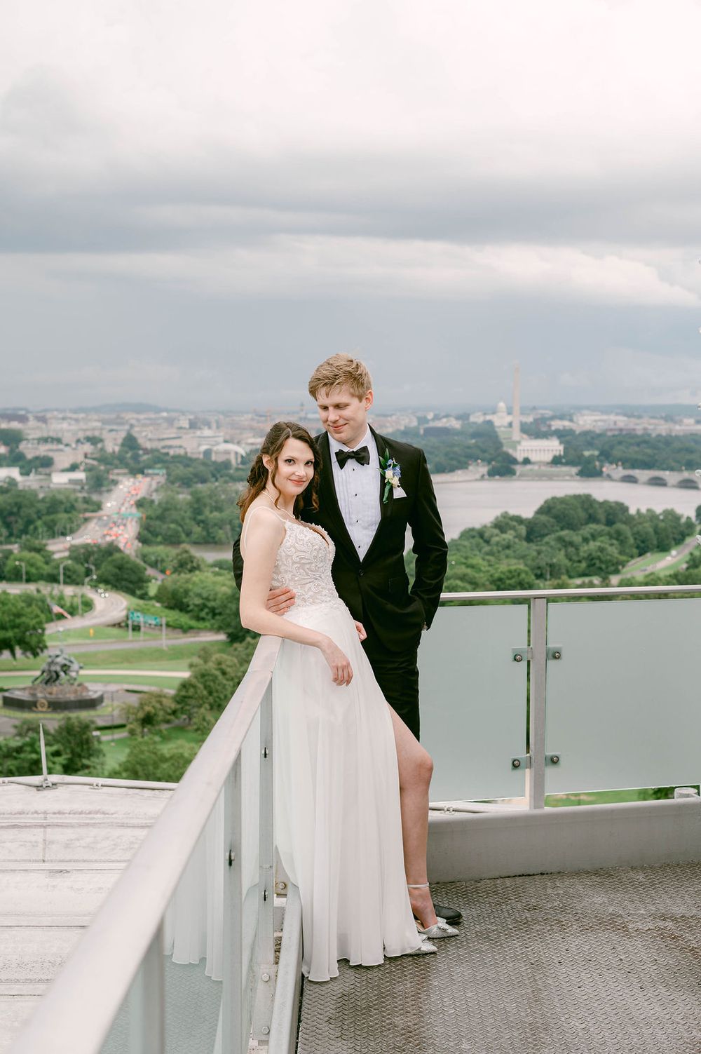 Wedding couple poses on outdoor terrace overlooking city skyline and water.