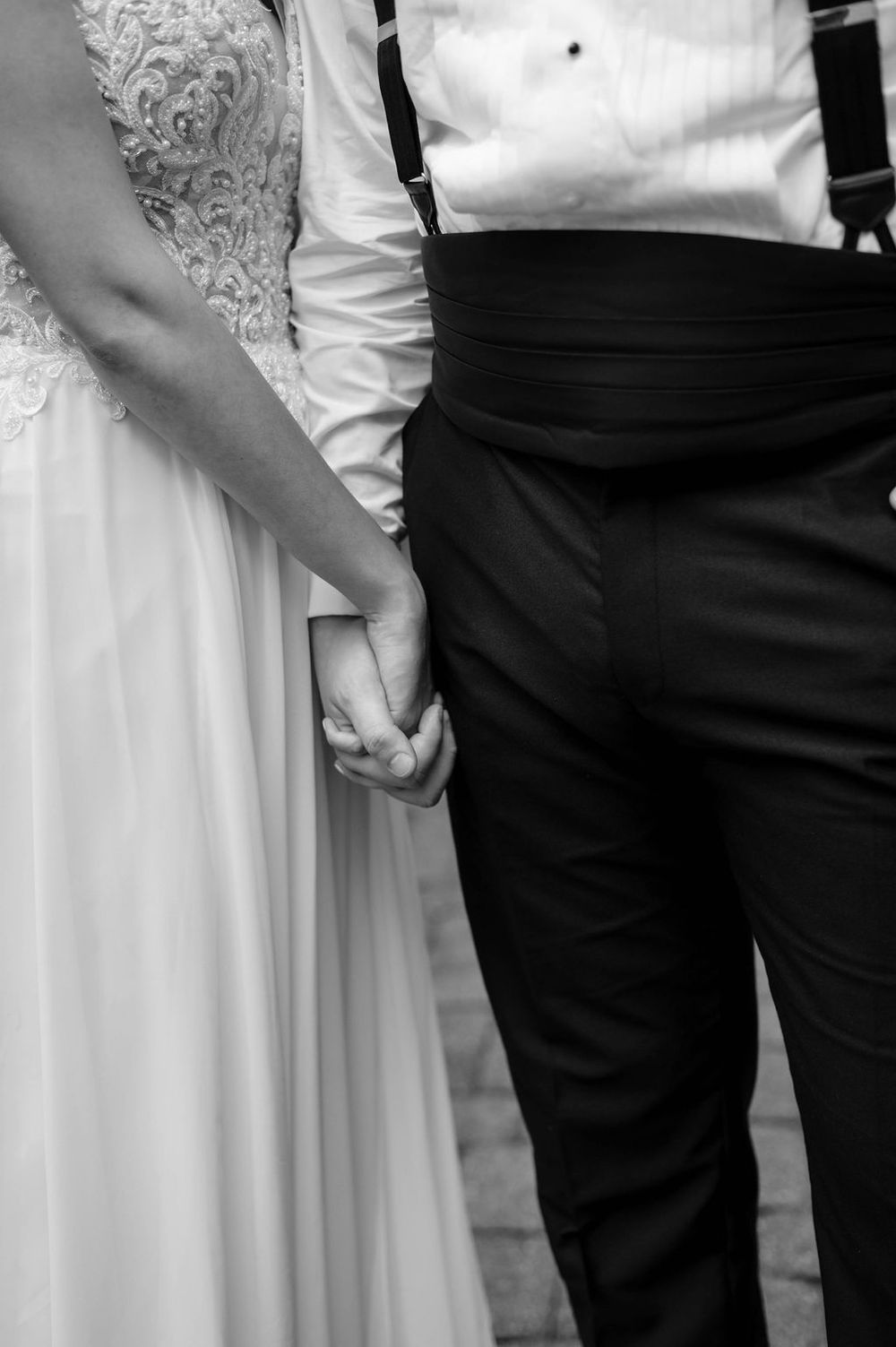 A black and white photo showing a couple holding hands on their wedding day, with formal attire visible.