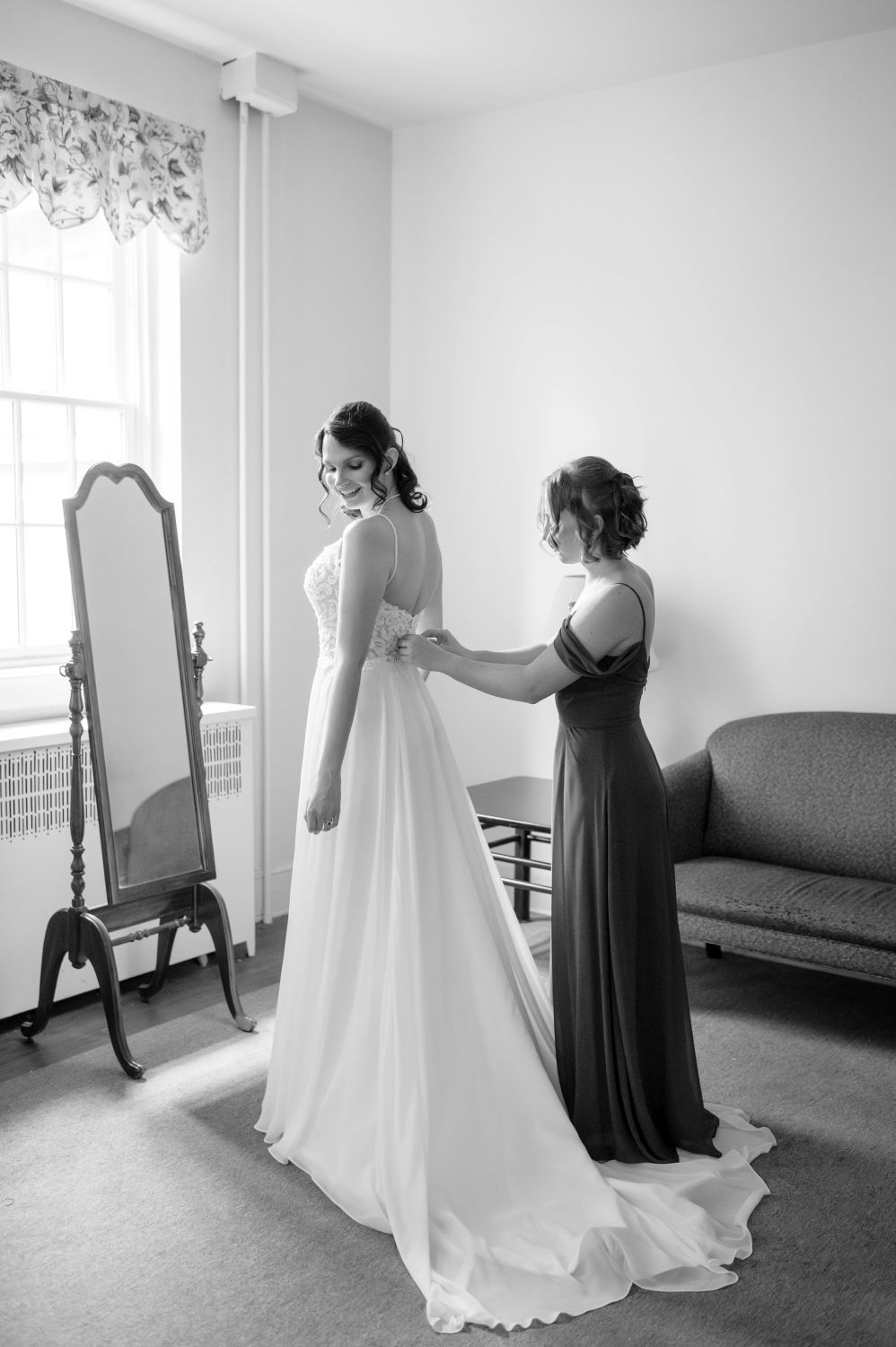 A series of black and white photos showing someone getting dressed in a flowing white wedding gown with assistance.