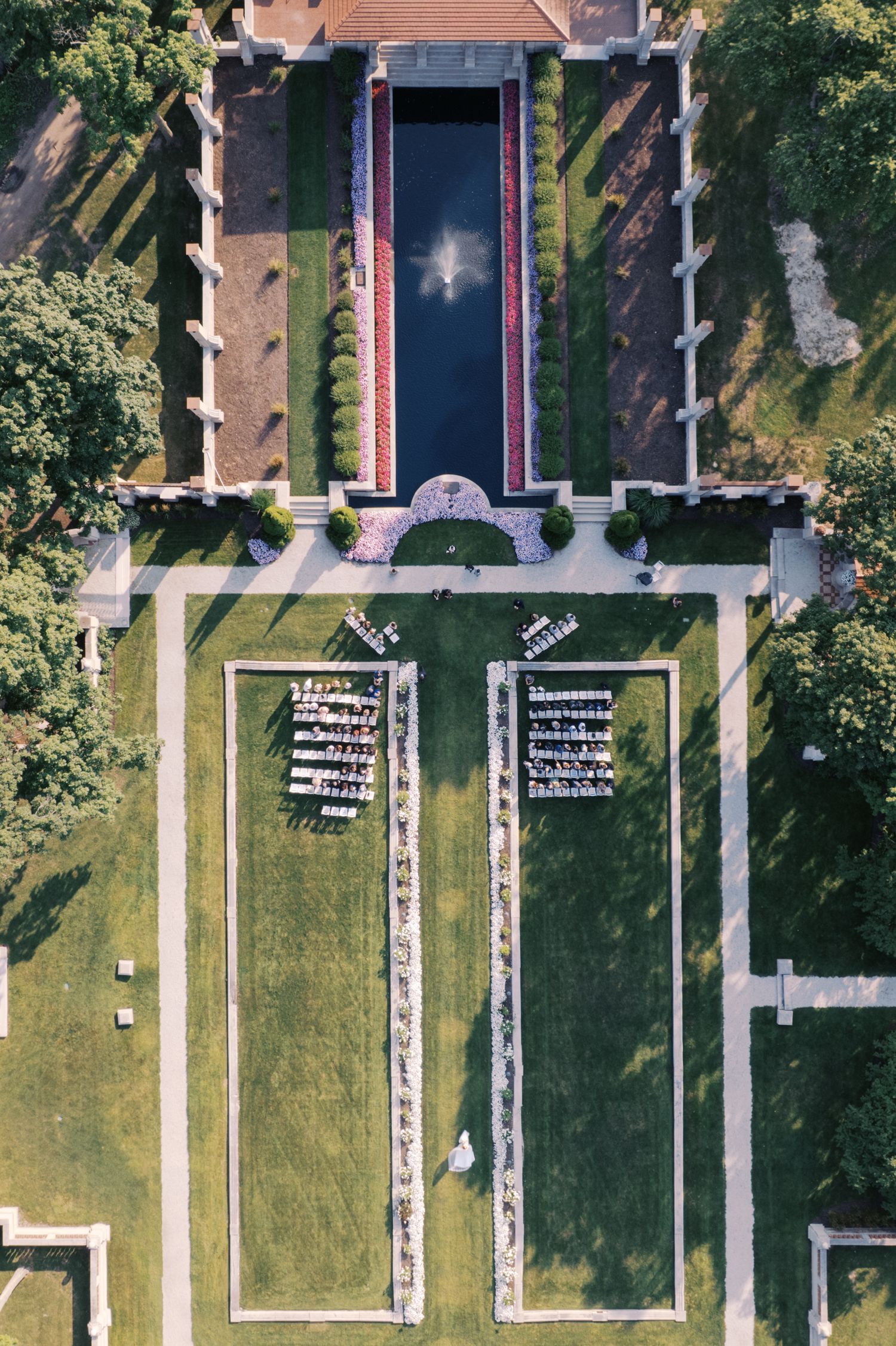 Aerial view of military cemetery with rows of white headstones and green lawns surrounded by trees.