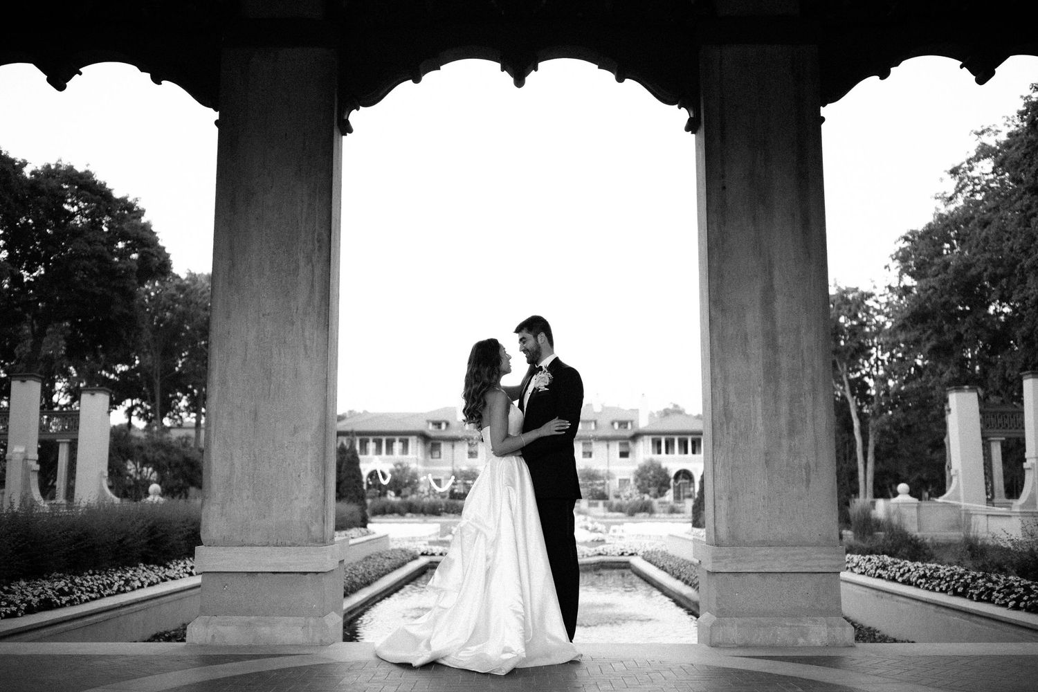 Romantic silhouettes under stone columns with elegant wedding attire at sunset.