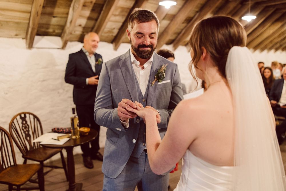 Wedding guests socialize and enjoy drinks at an indoor reception venue with rustic wooden beams and warm lighting.