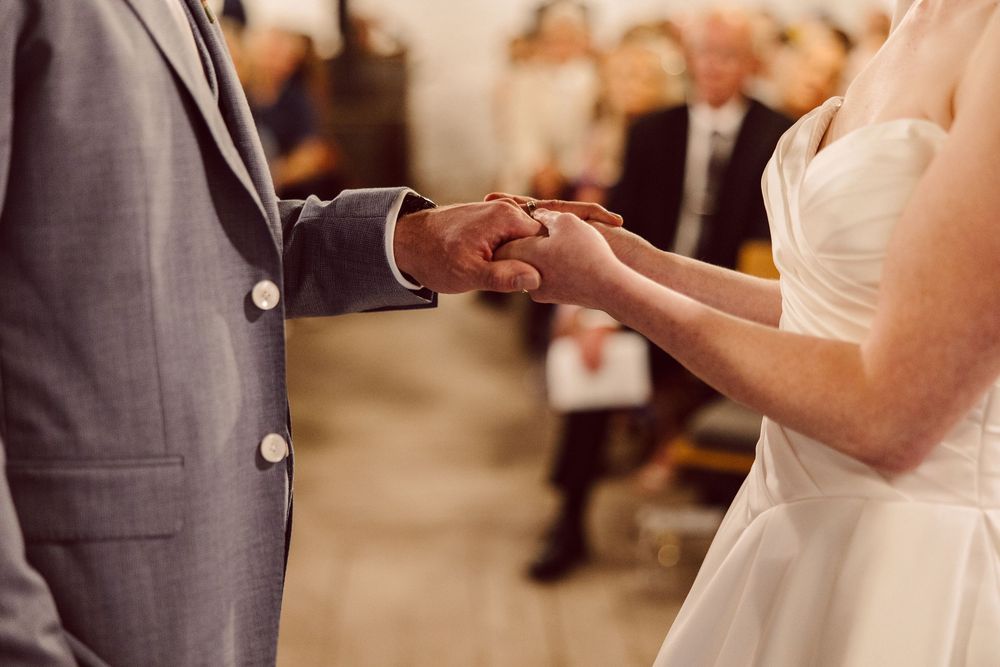 A couple in formal wedding attire exchanges rings during an outdoor ceremony.