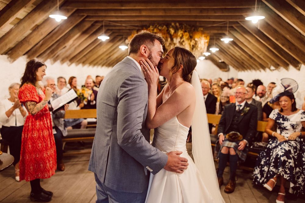 A romantic wedding celebration in a rustic barn venue with warm lighting and guests watching the couple dance.