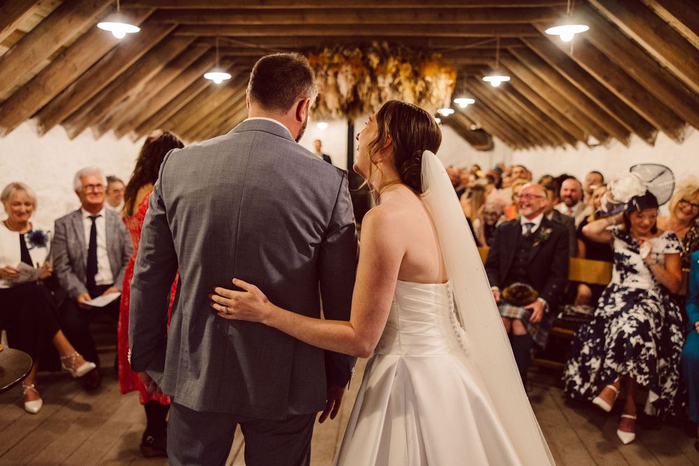 Guests dancing and celebrating at a lively wedding reception in a rustic barn venue with wooden beams and warm lighting.