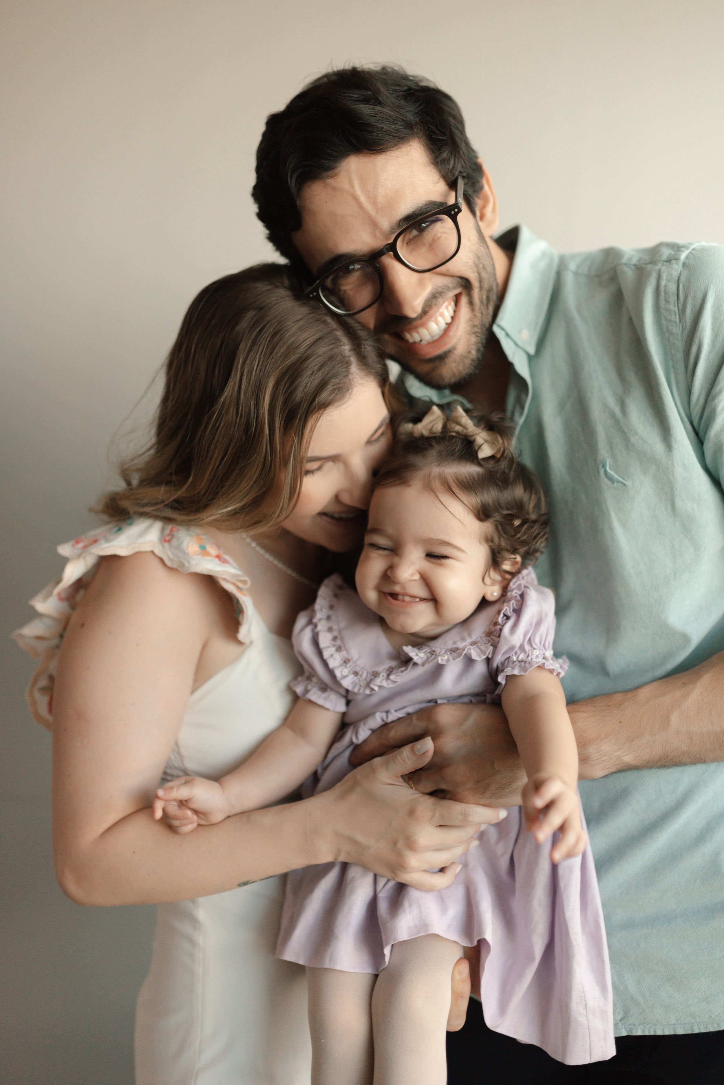 A family of three shares tender moments together in a series of candid photos wearing light colored clothing.