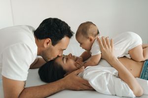A couple shares an intimate moment together while lying in bed with white bedding.