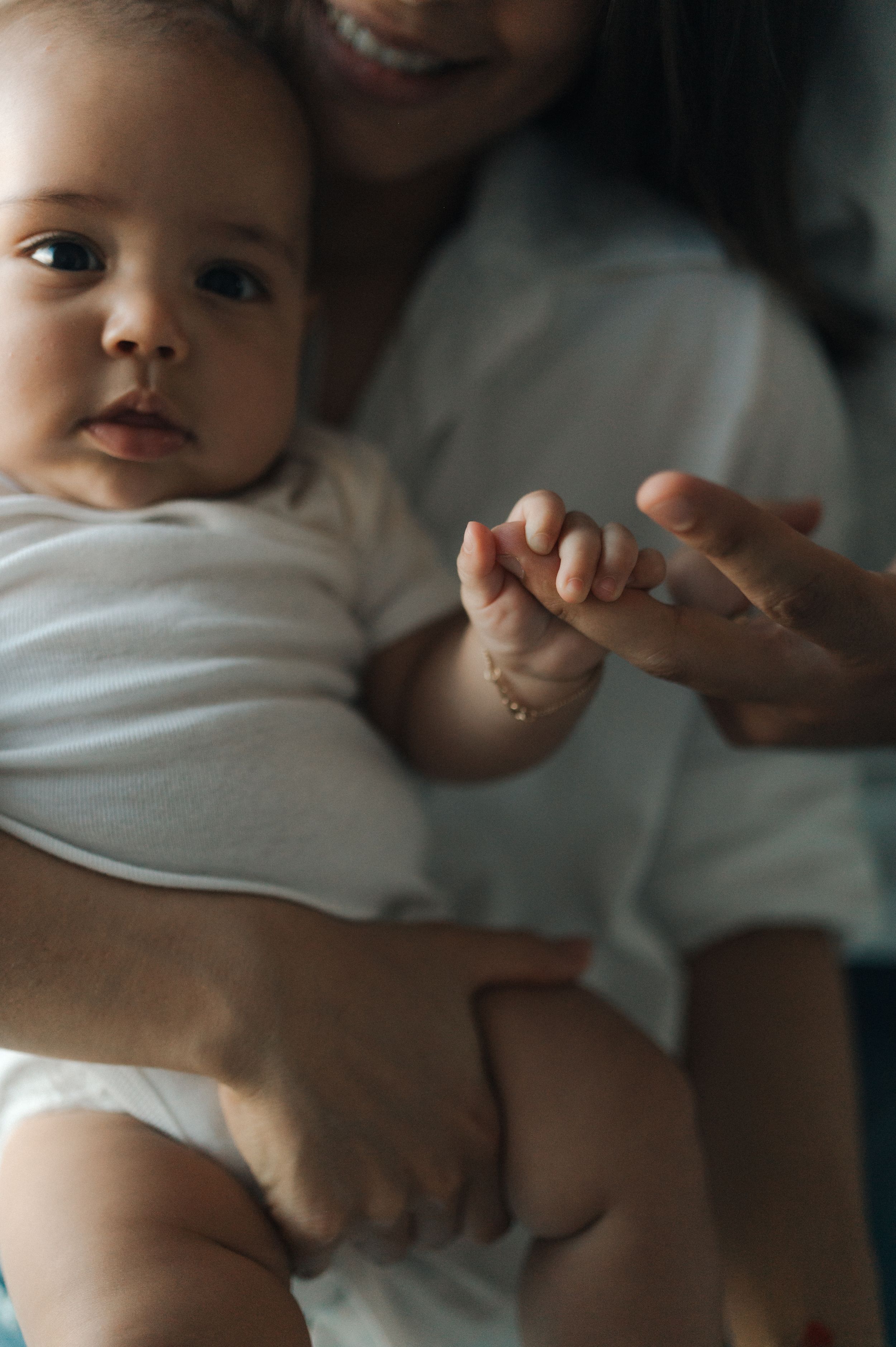 Close-up photos showing tender moments between a baby and caregiver's hands against a soft neutral background.