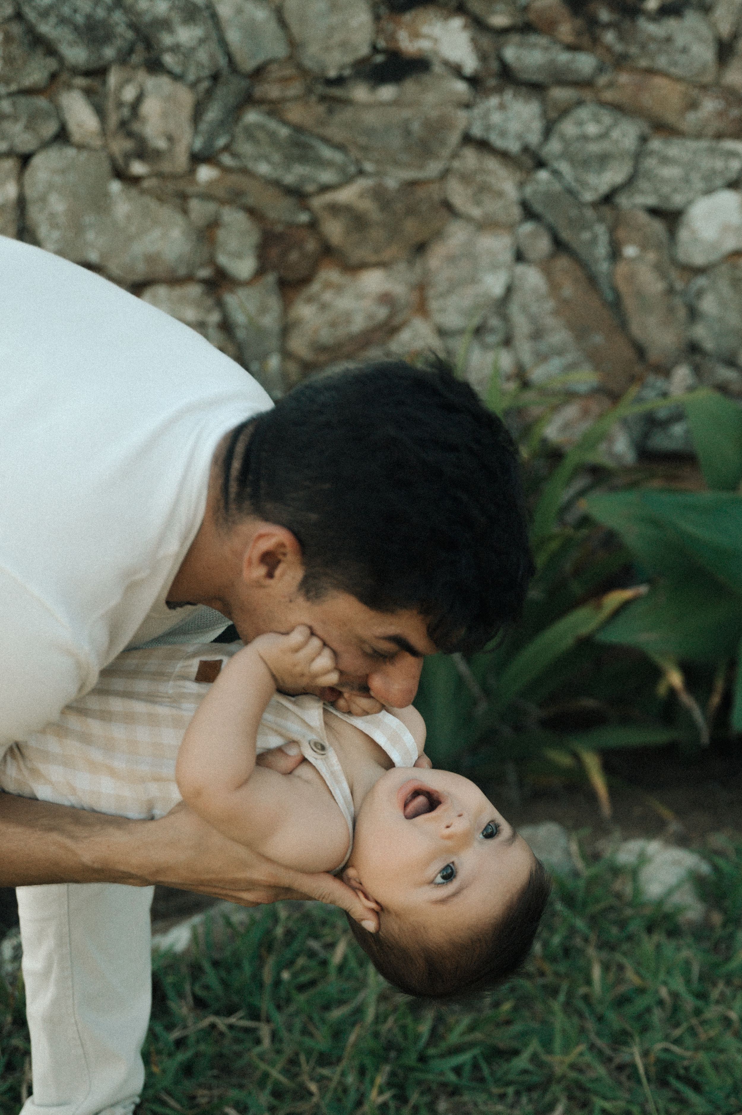A series of three tender moments captured between parent and child playing outdoors against a stone wall.