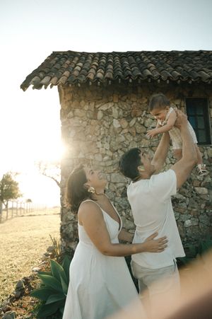 Two people in white outfits dance together against a rustic stone wall backdrop during golden hour.