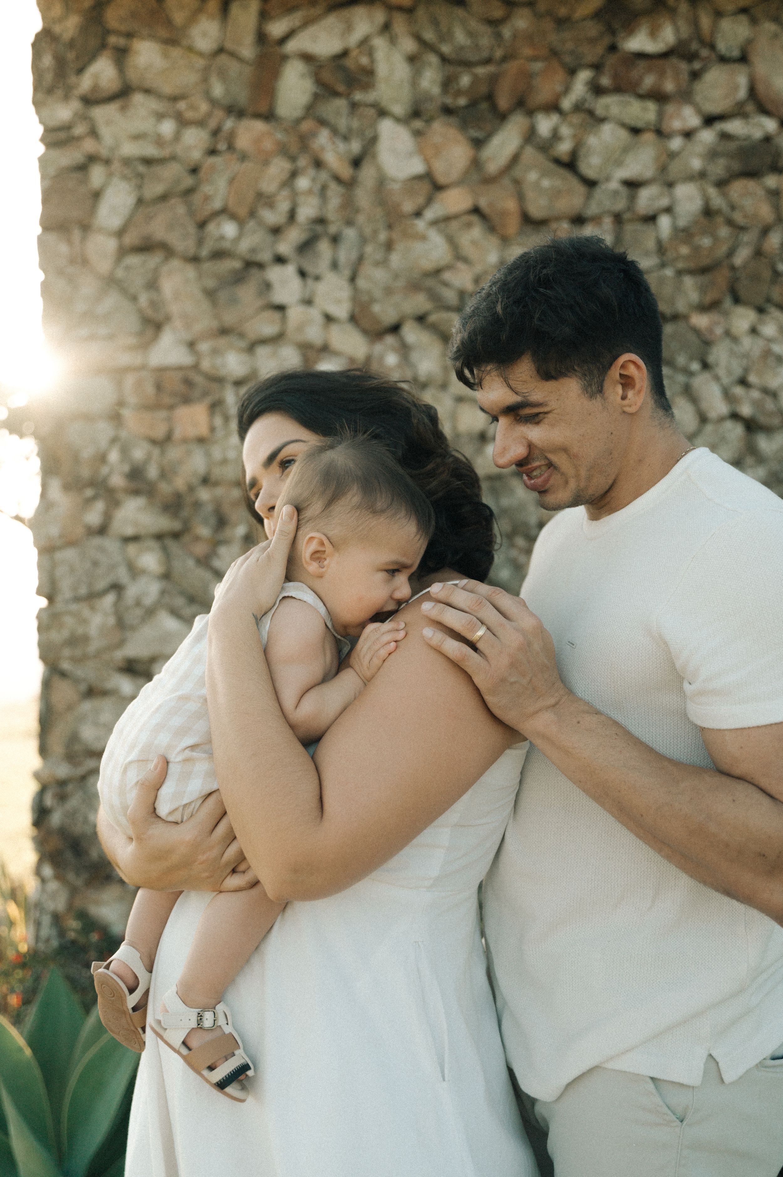 A tender family moment captured in a series of four intimate photos against a rustic stone wall in warm sunlight.