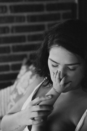 Black and white portrait of a person with curly hair in an intimate, emotional moment against a brick wall.