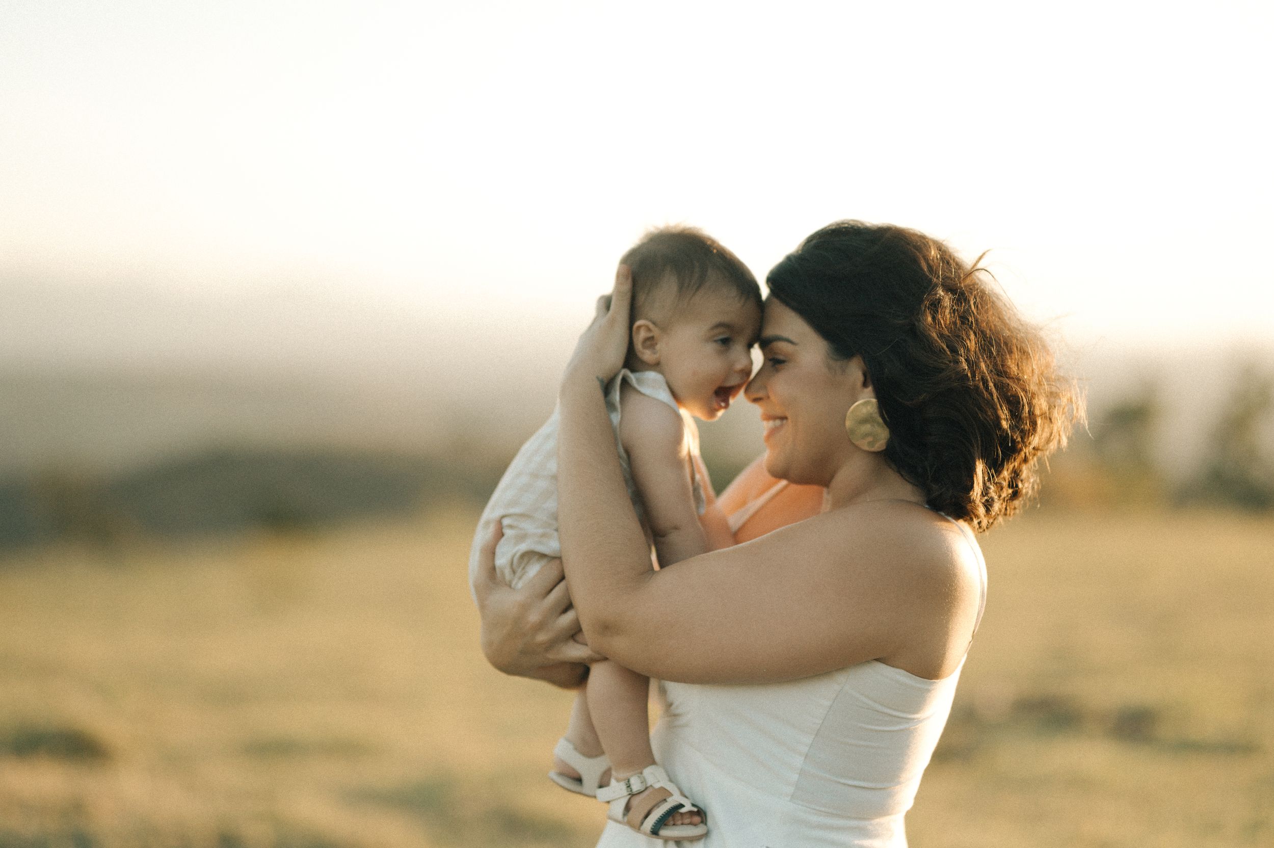 A romantic couple embraces during golden hour in a field as sunlight creates a warm, dreamy atmosphere.