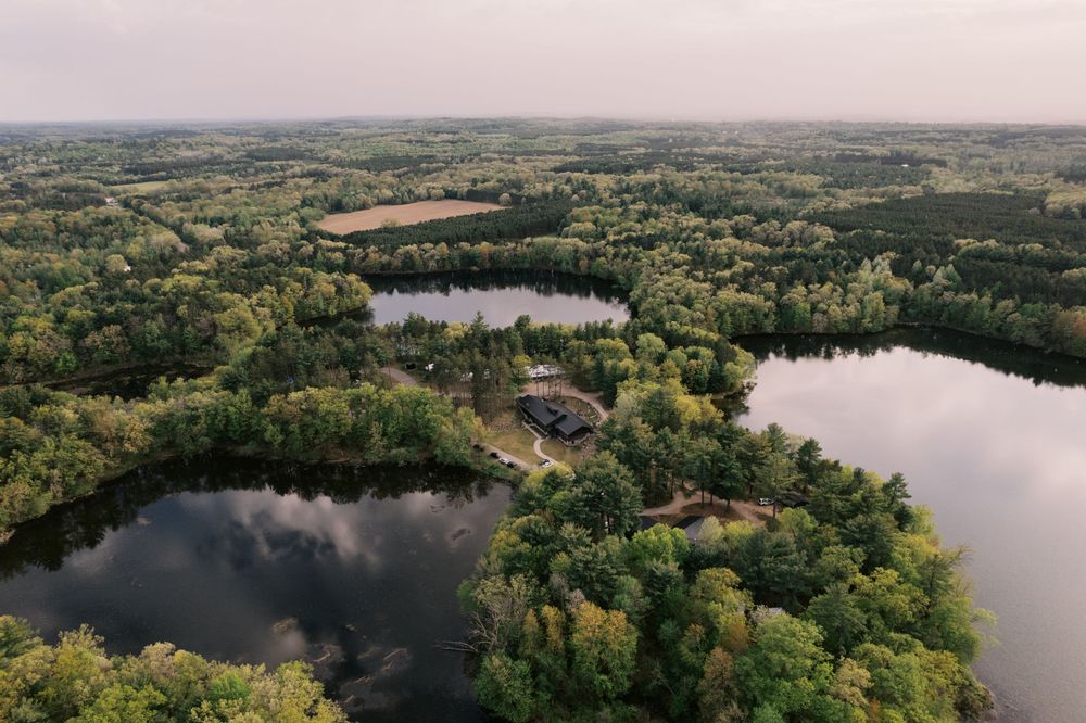 Aerial panoramic view of a scenic lake surrounded by lush green forests and farmland stretches into the horizon.