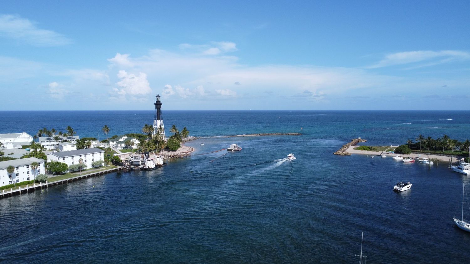 Aerial view of Hillsboro Lighthouse in Florida with turquoise waters and boats entering the inlet.