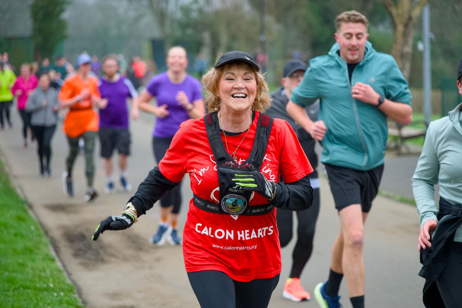 Enthusiastic runner participating in parkrun event wearing red shirt and cap.