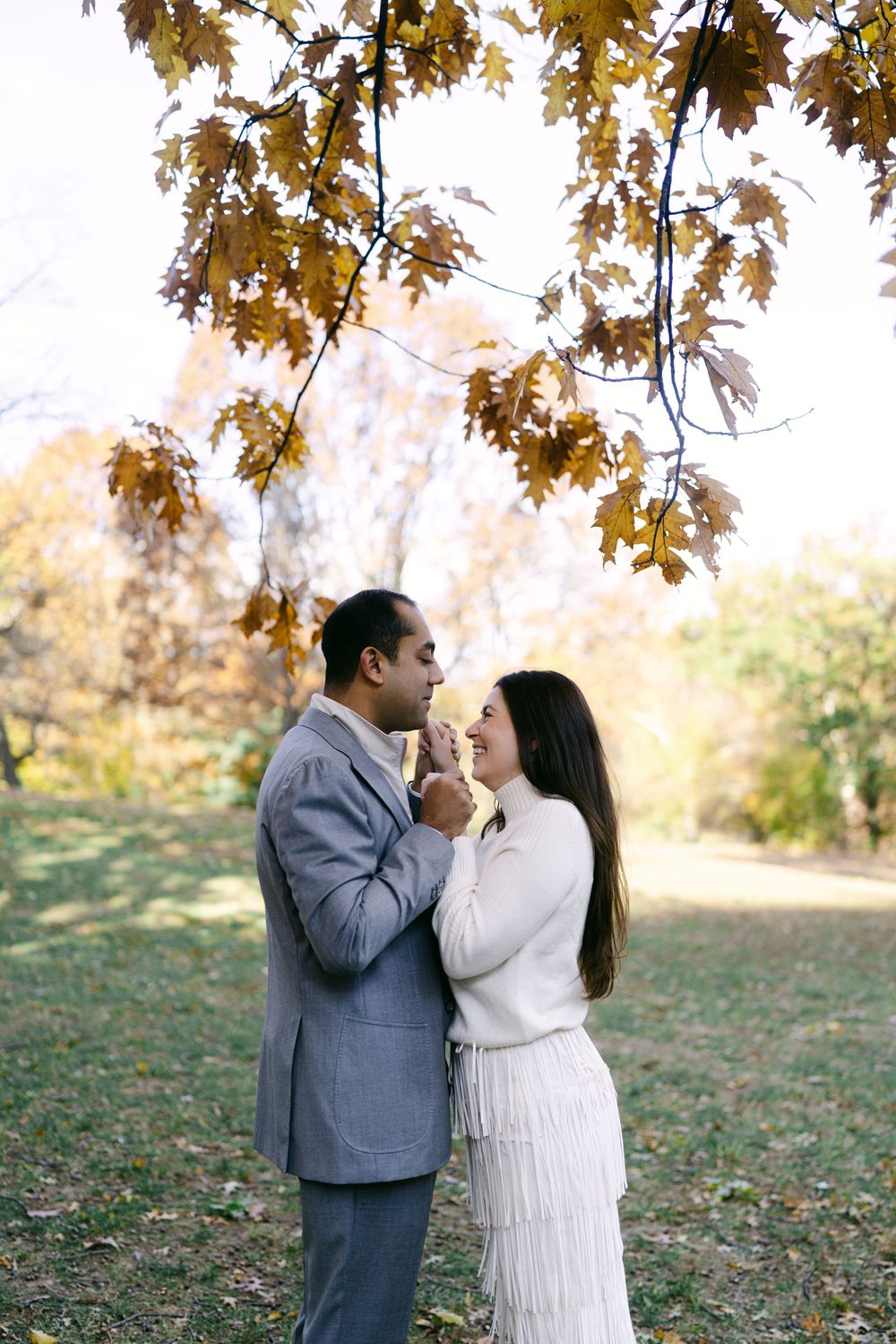 A couple shares a tender moment under golden autumn leaves in a romantic outdoor photoshoot.