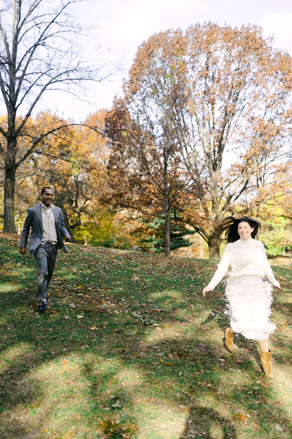 Two people dance and twirl together on a leaf-covered slope during fall.