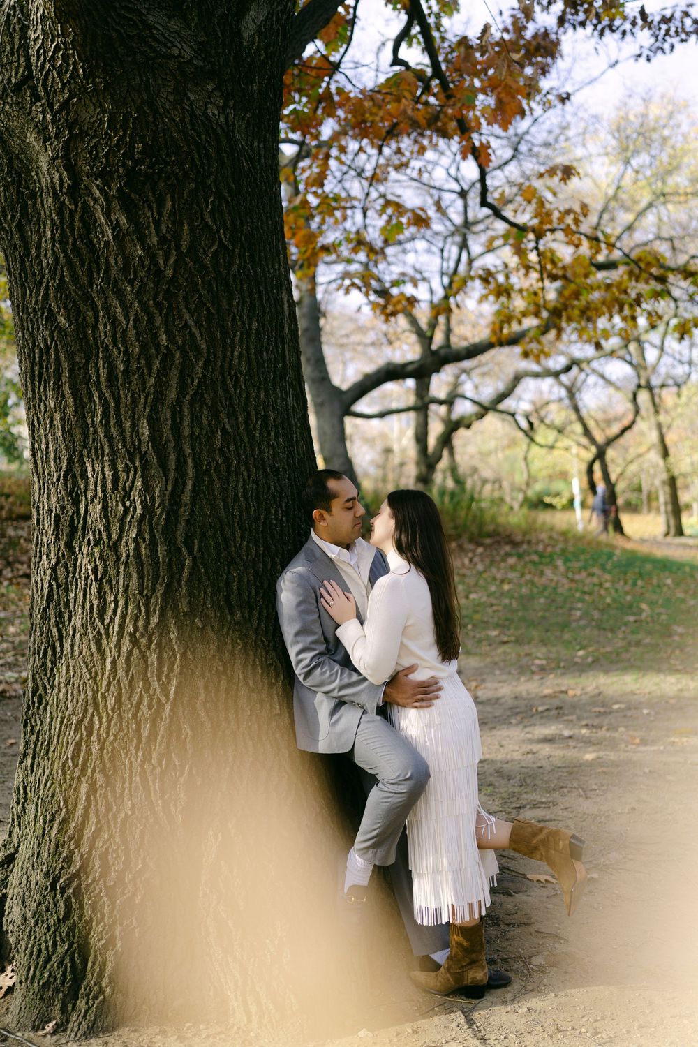 A romantic moment captured between two people leaning against a massive tree trunk.