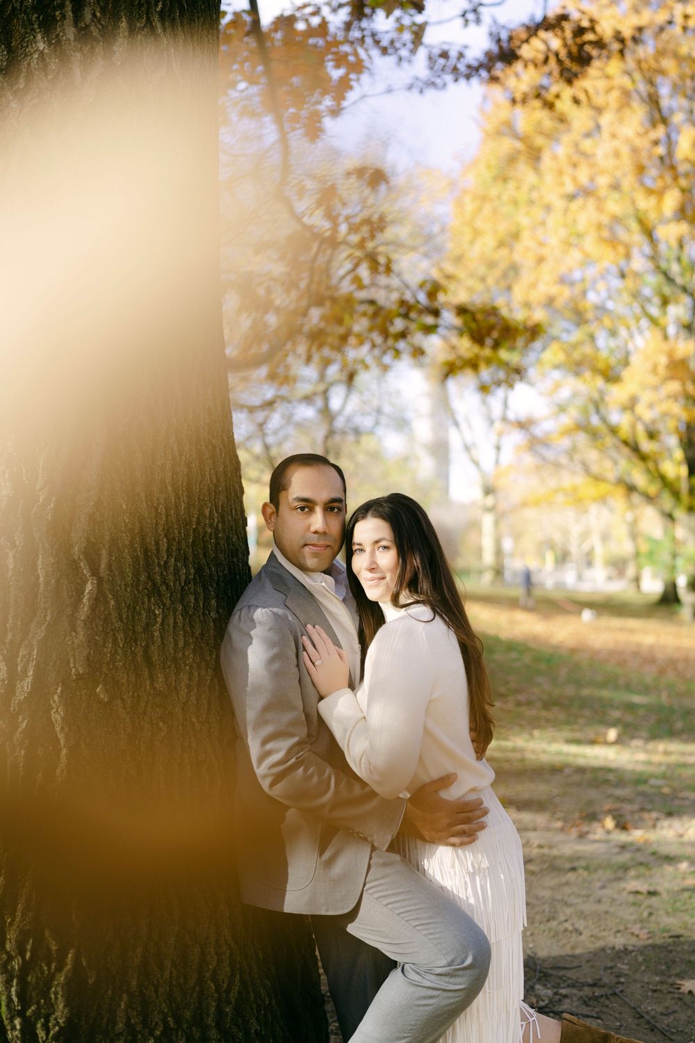 Romantic outdoor autumn engagement photos with golden sunlight filtering through trees in a park setting.