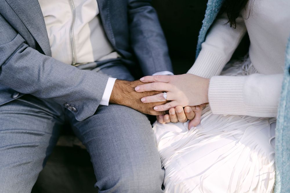 Close-up shot of hands with engagement ring showing couple holding hands in formal wedding attire.