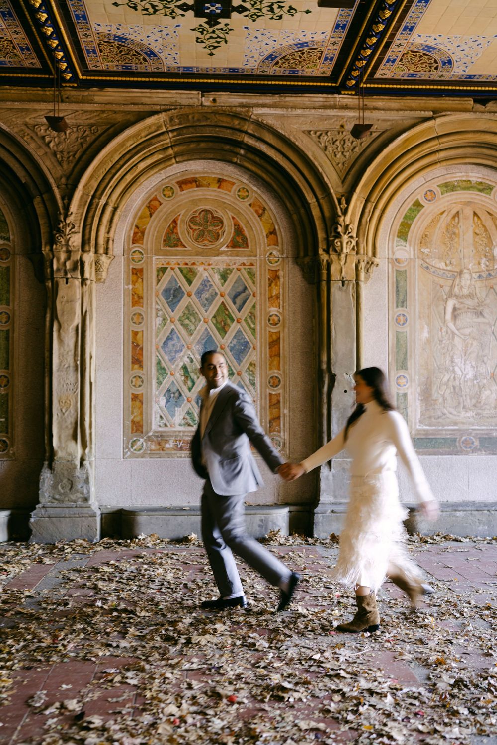 Two figures in motion dance across a decaying ornate room with debris scattered on the floor and decorated walls.