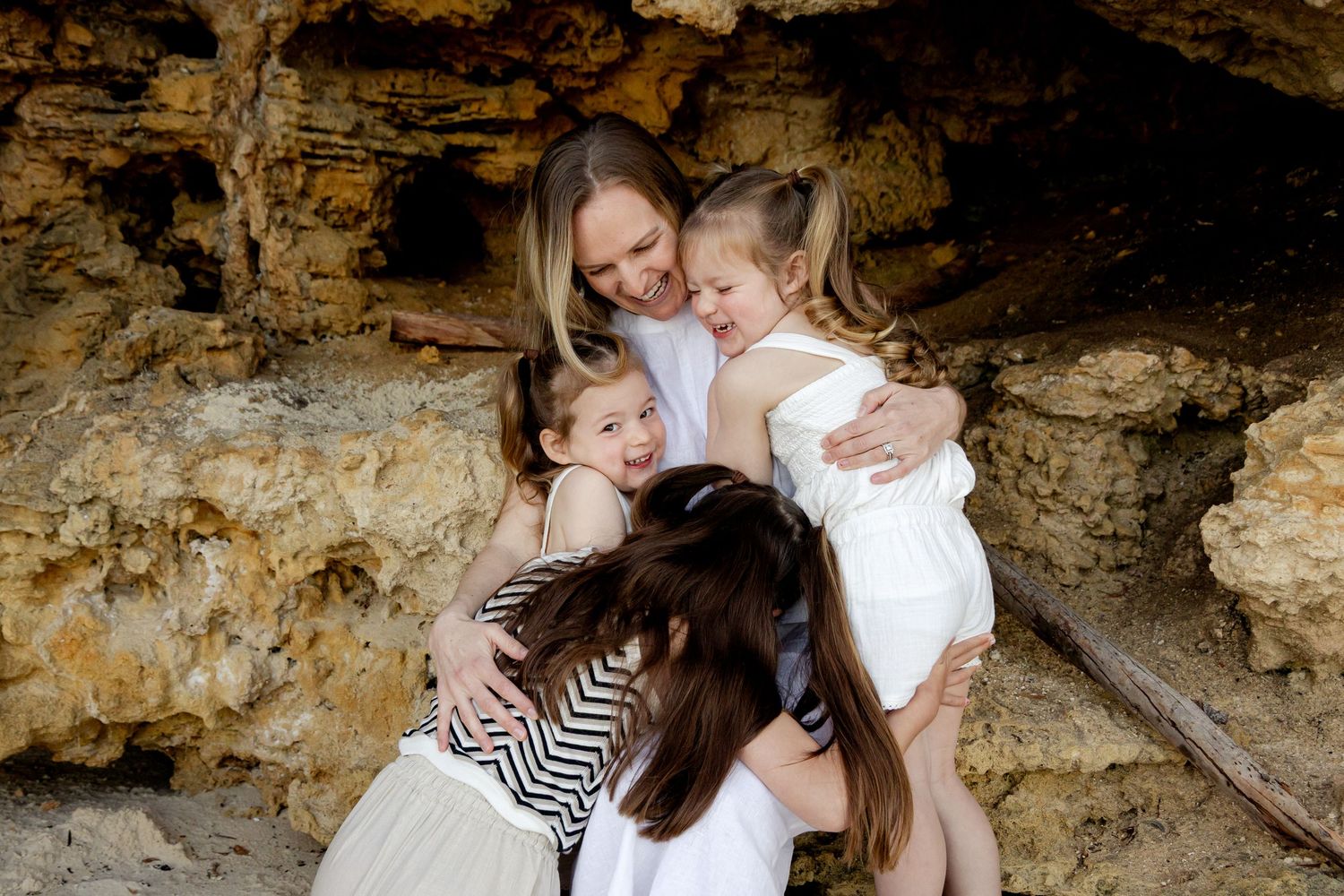 A tender family moment captured in a rustic cave-like setting with natural stone walls and warm lighting.