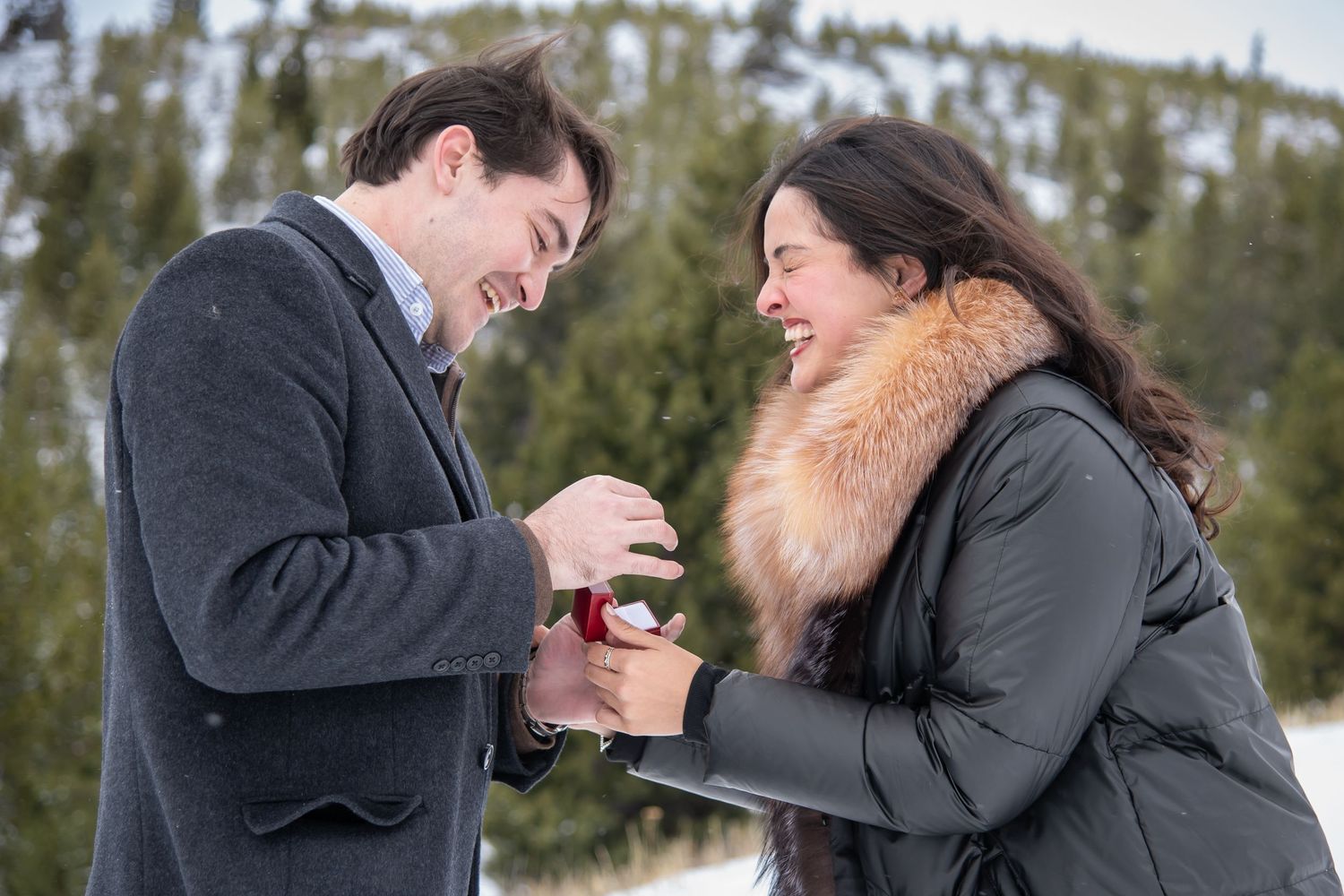 A cute and very happy couple candidly after a surprise proposal at Sapphire Point Colorado with snow and trees around them.