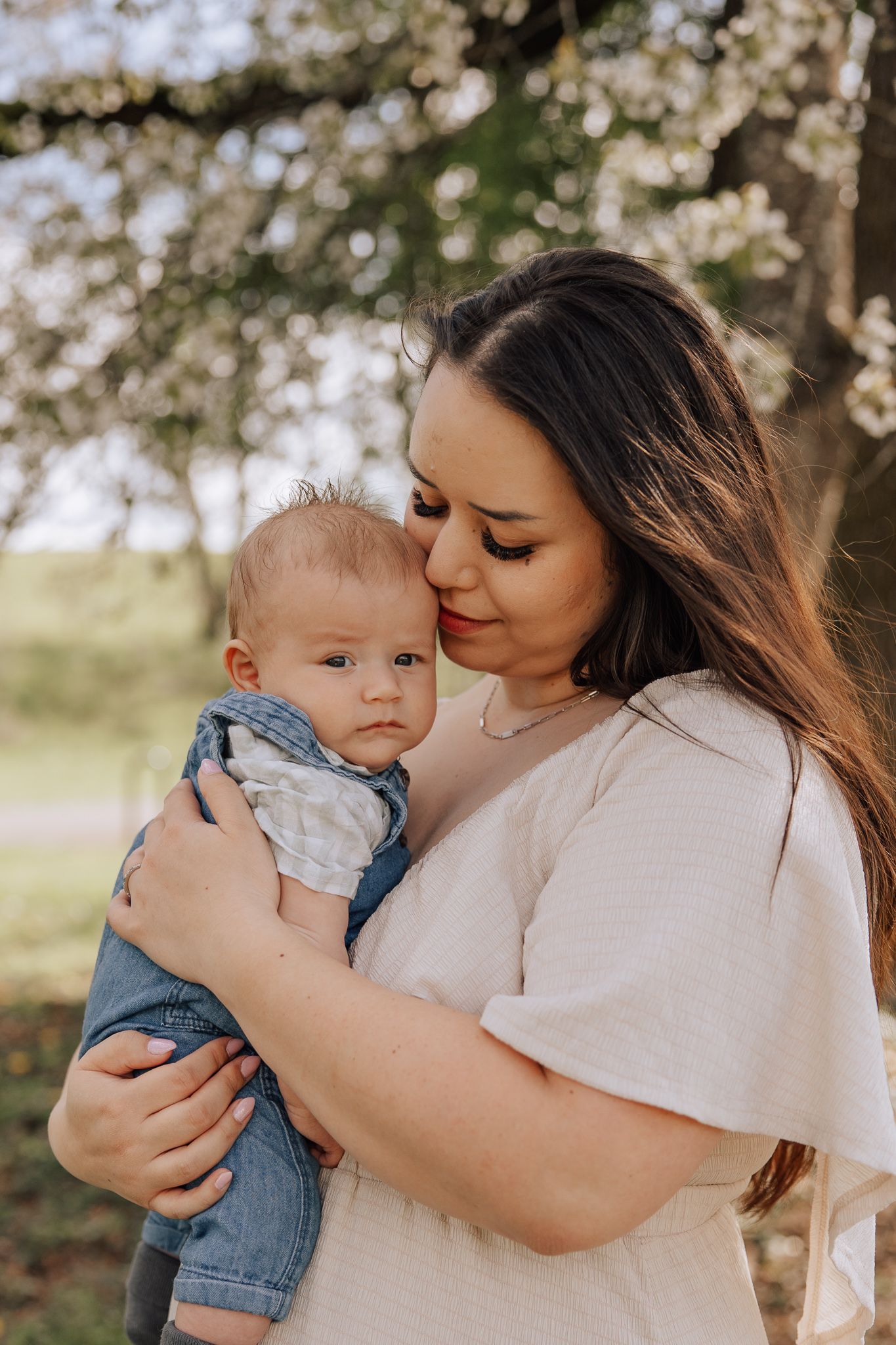 A smiling mother holds her young son at golden hour in an open green field at sunset.