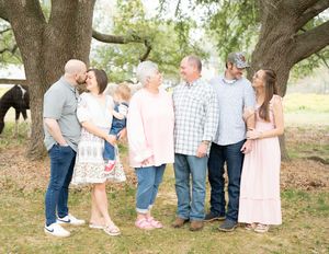 Family group poses together under large oak tree in outdoor portrait session wearing coordinated pink and blue outfits.