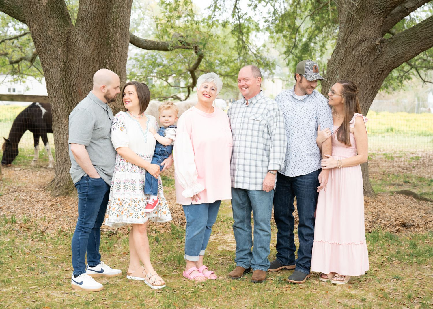 Family gathering beneath sprawling tree branches in natural outdoor setting with matching casual attire.