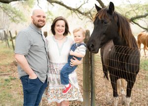 Family members interact with a black horse through a wire fence on a sunny day.
