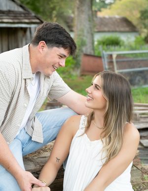 A couple in casual white attire shares romantic moments while sitting outdoors in a natural setting.