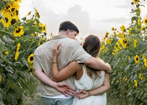 A romantic couple embraces in a field of tall blooming sunflowers during golden hour.